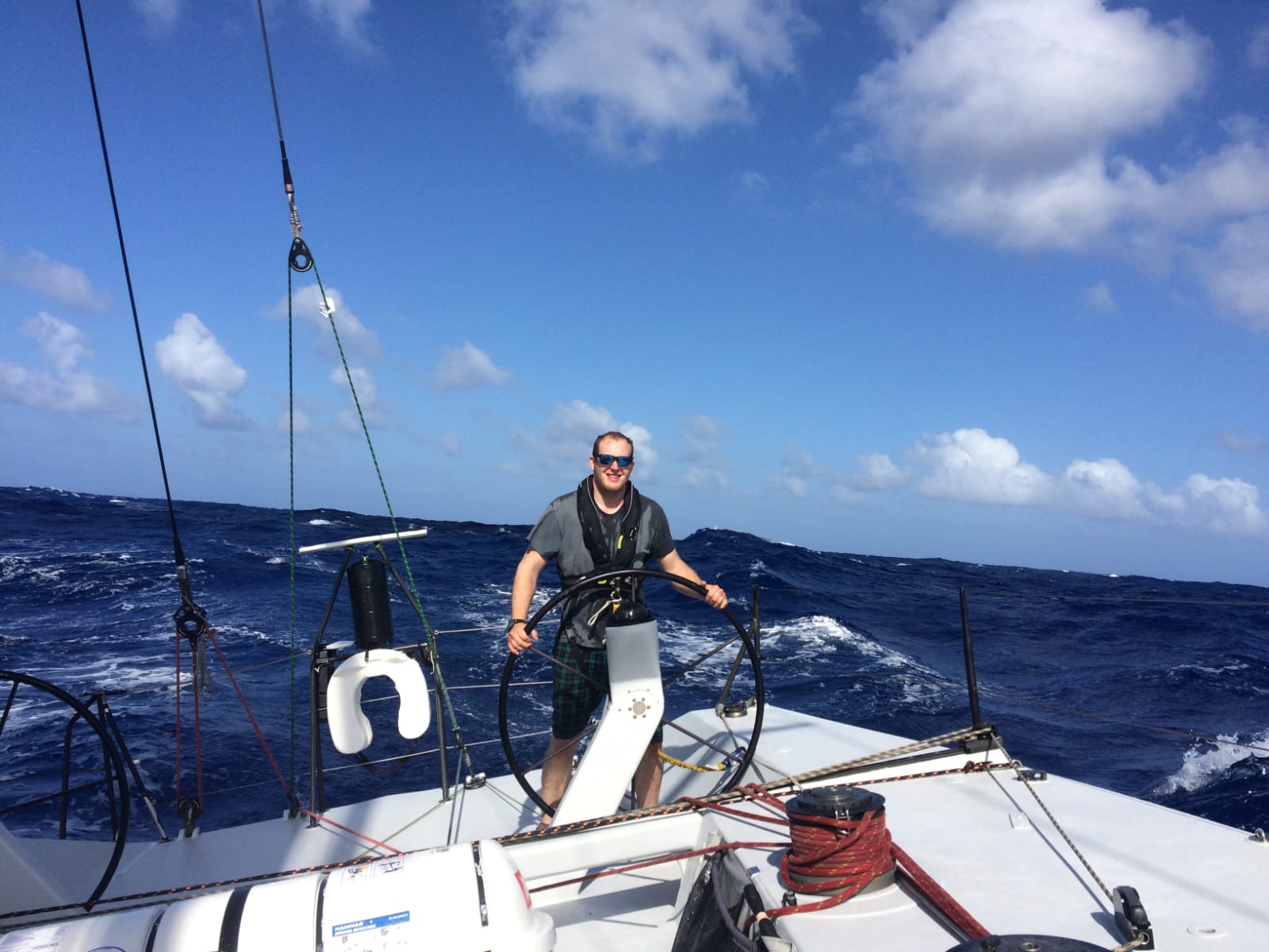 Ken at the helm of Challenger approaching Antigua on day 11, blue sky and deep ocean behind him